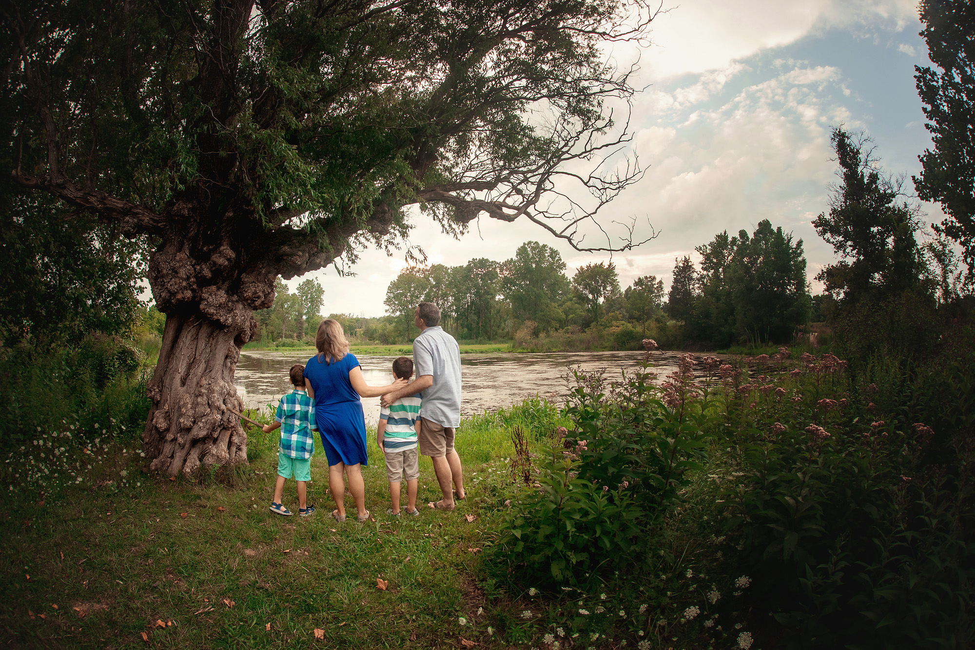 family of four looking at lake by tree