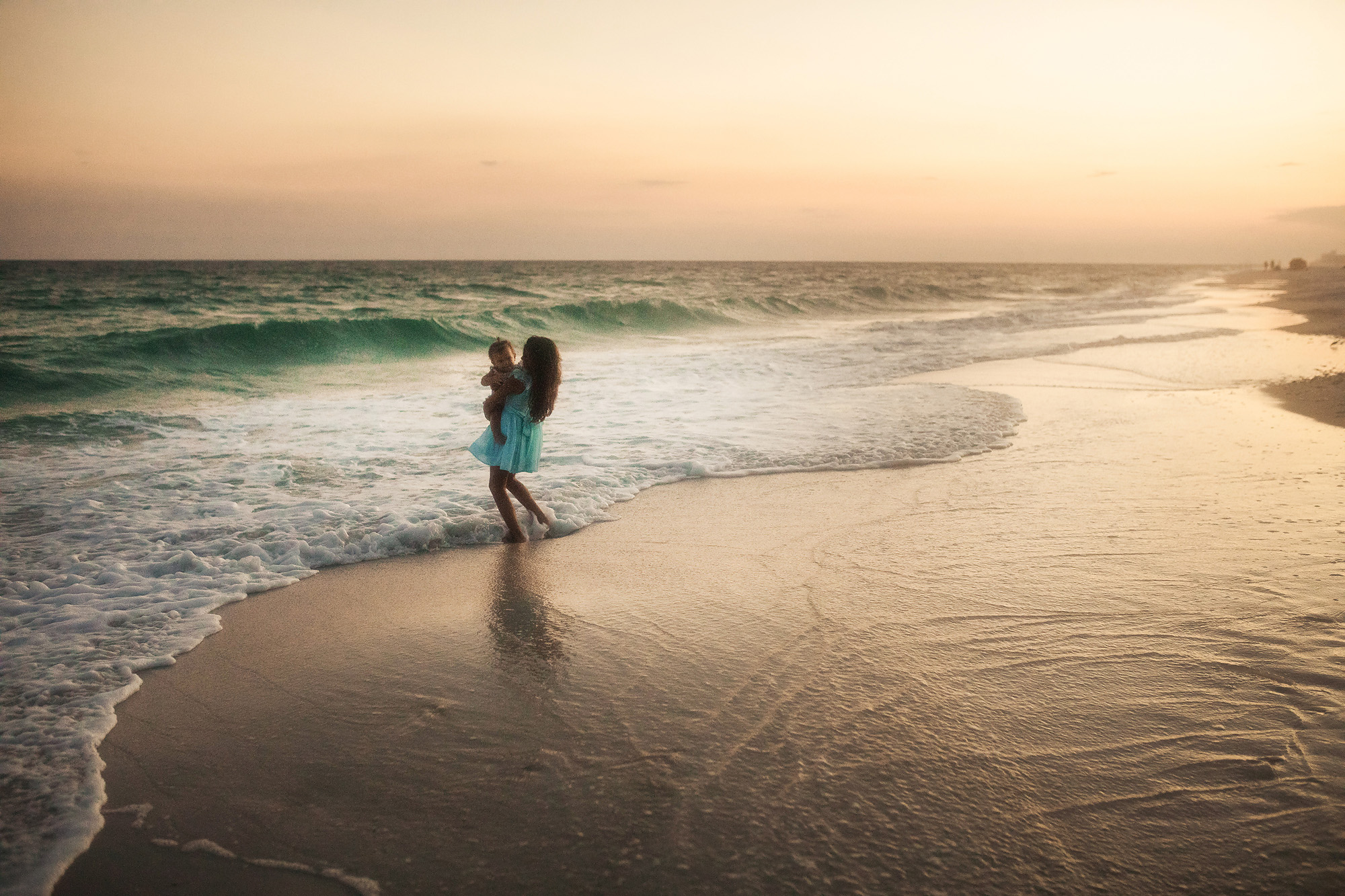 girl holding sister by ocean waves