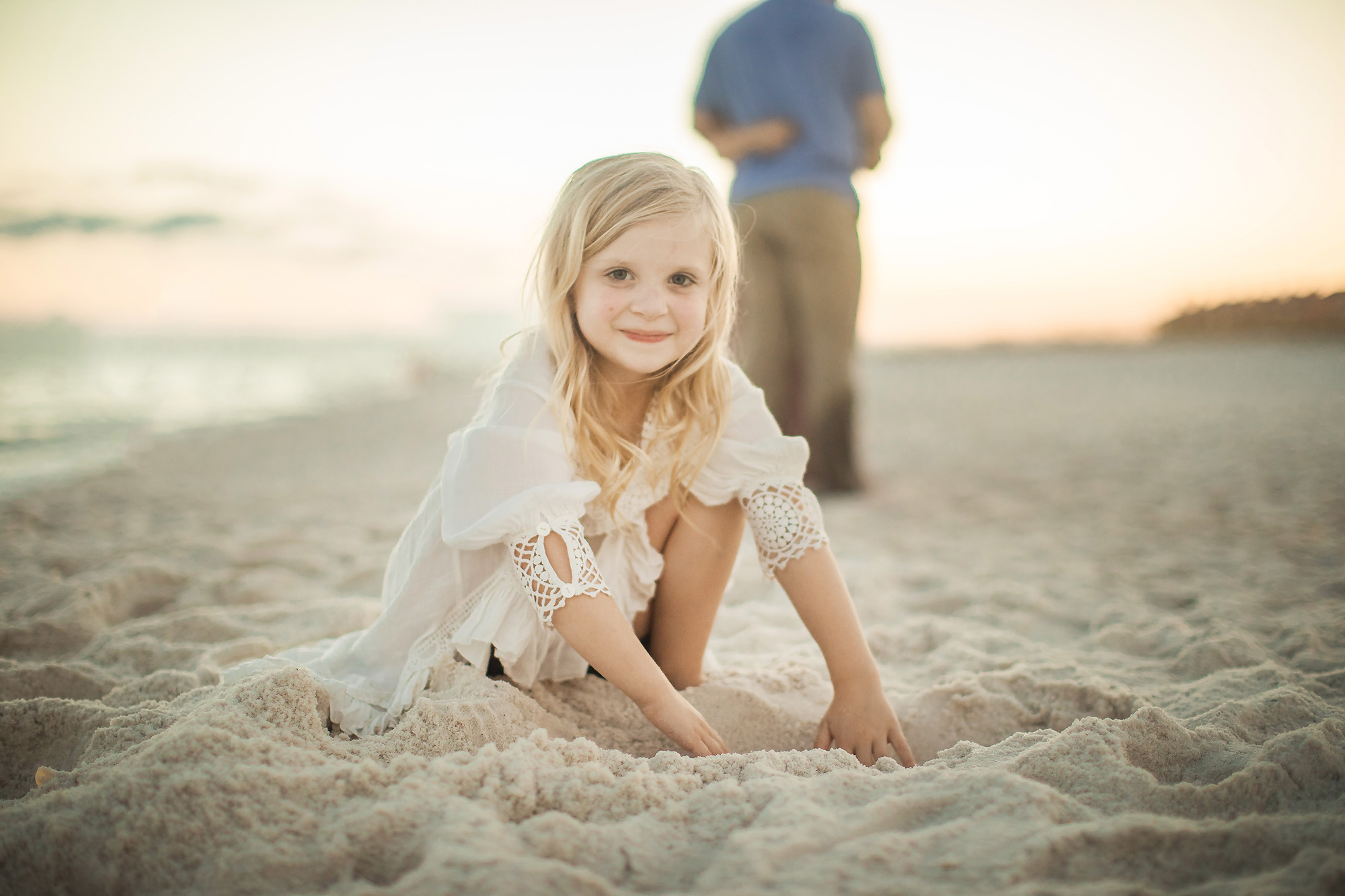girl playing in sand dad in back
