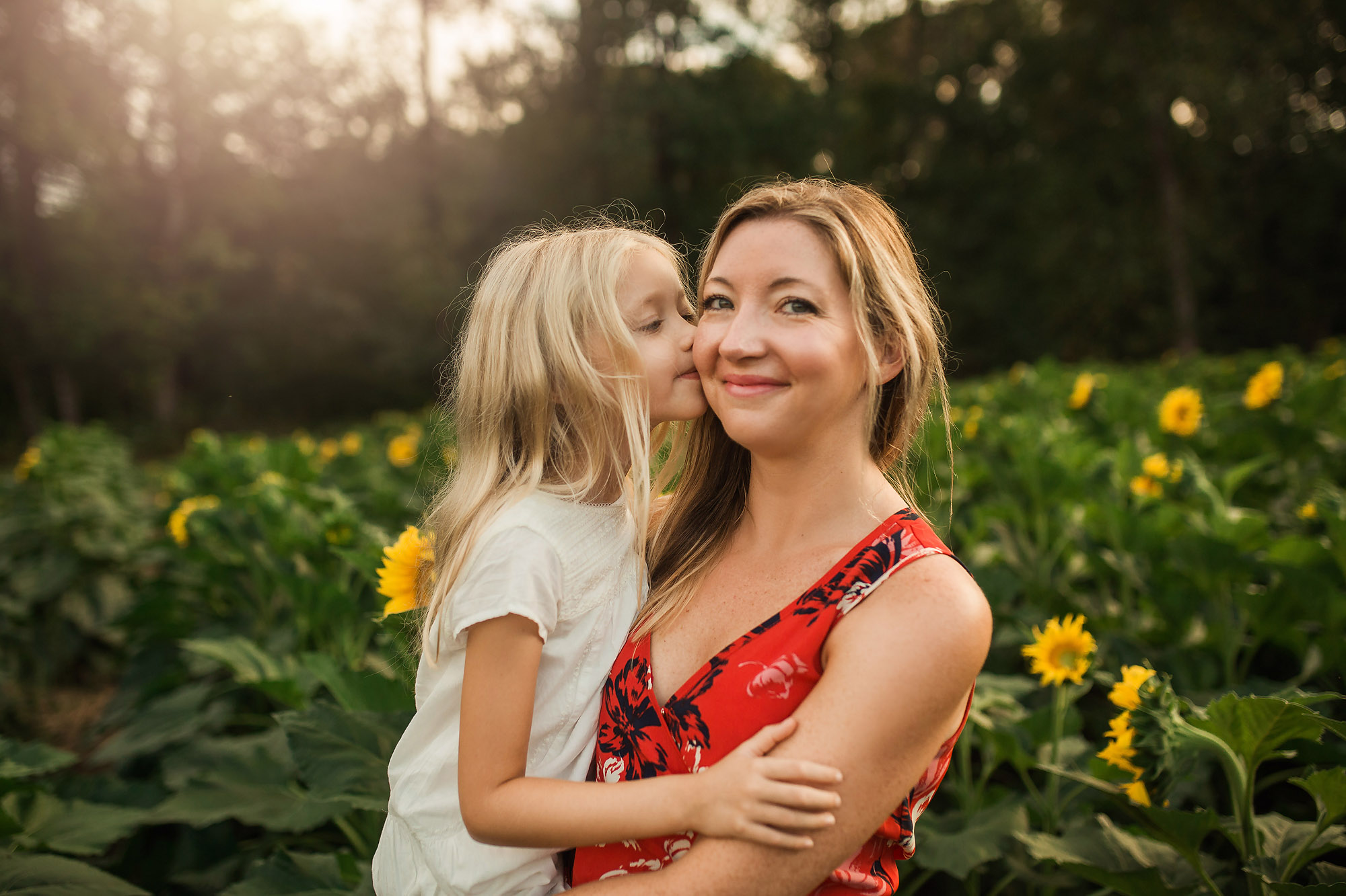 girl kissing mother by sunflowers