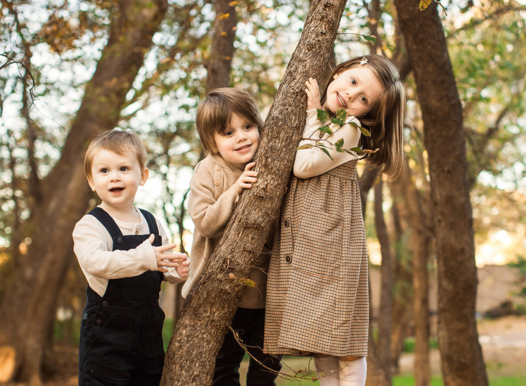 three siblings playing by tree