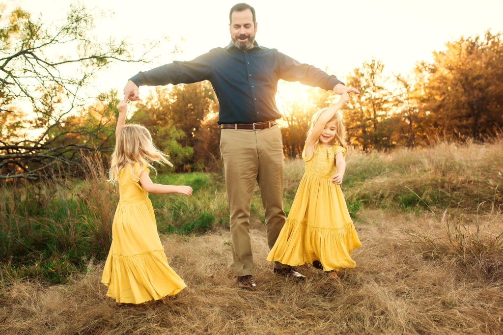 father spinning twin daughters in sunshine