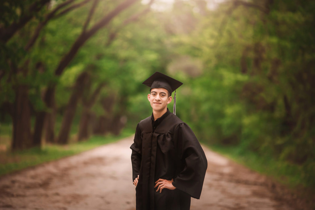 senior boy in cap and gown outdoor path