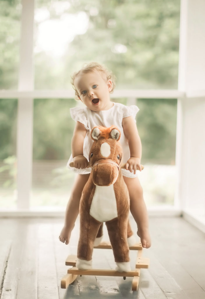 baby girl on toy horse on porch