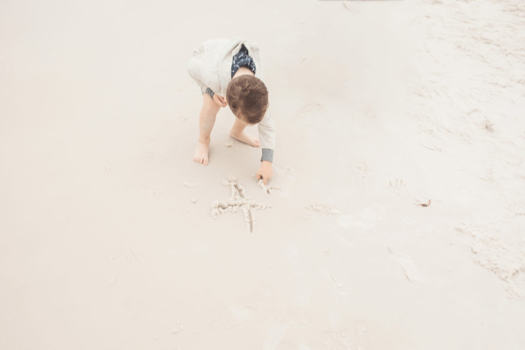 boy writing name in white sand beach