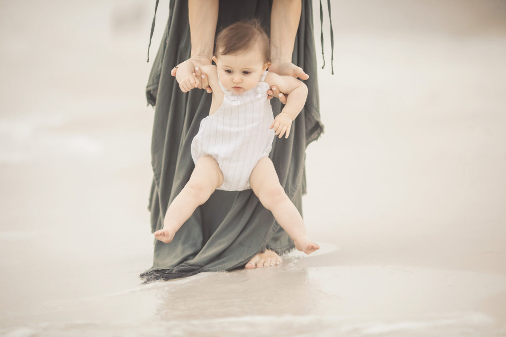 mom putting baby girl in sand