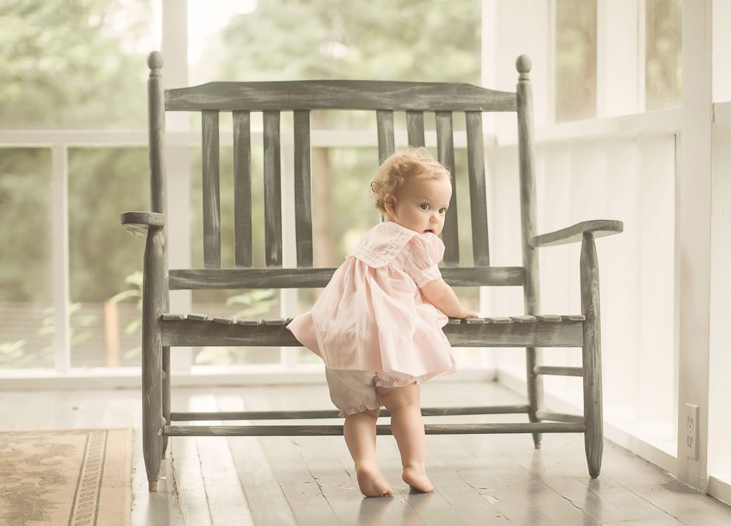 baby girl in pink dress by green bench