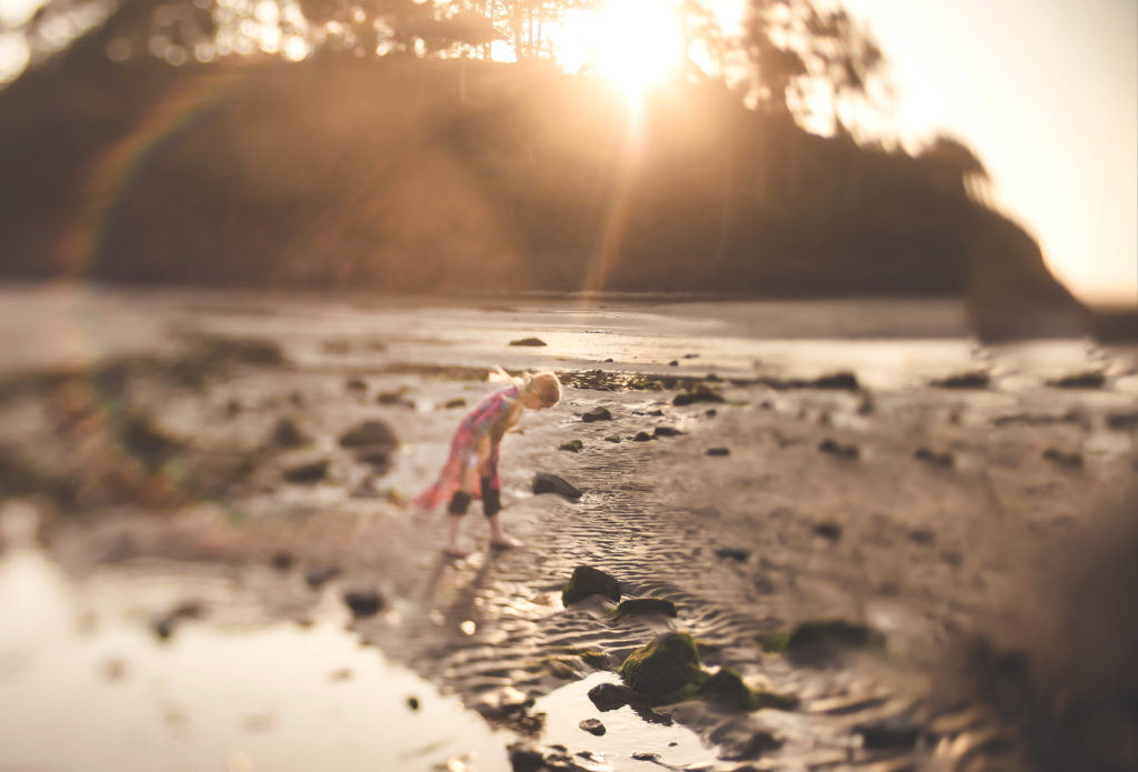 girl on beach collecting rocks lensbaby