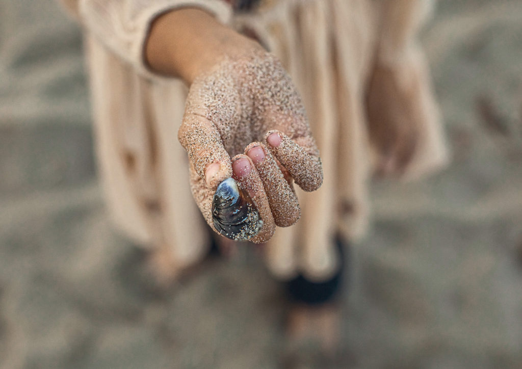 girl with shell and sand on fingers