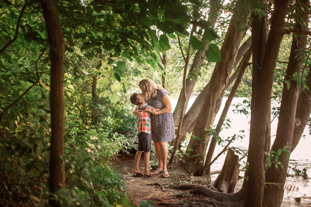 mother kissing son under trees by river