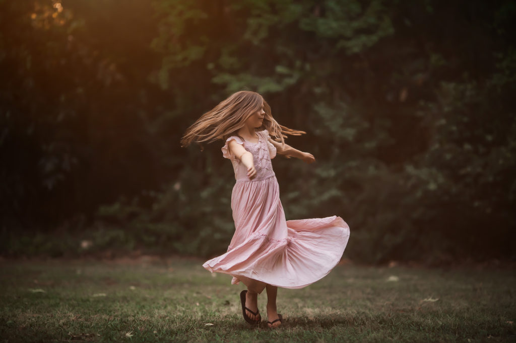 girl spinning in pink dress in grass