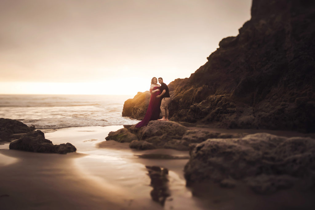 couple at sunset by rocks at beach