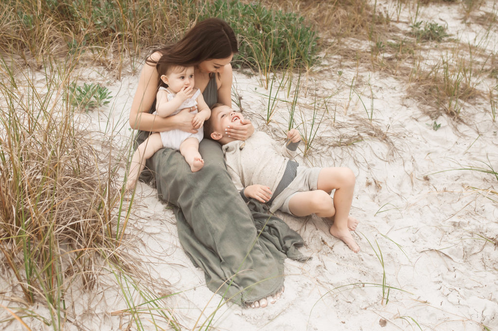 mother snuggling children on beach grass